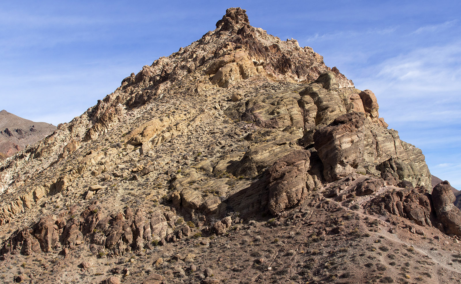 Detail of peak at Red Pass showing slanted strata of Titus Canyon Formation with shale and  sandstone topped by volcanic rock.